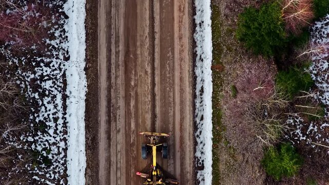 Yellow Grader leveling terrain for a new road, ground development in winter in aerial tracking shot