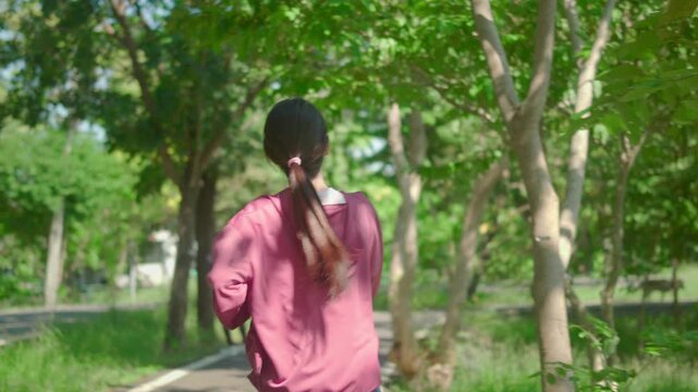 Rear view of young beautiful sport woman run in public park after exercise outdoors. Asian athlete beautiful girl exercises outside jogging workout outdoor for health and wellbeing in garden.