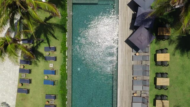 Beachfront resort in Ta&iacute;ba S&atilde;o Gon&ccedil;alo do Amarante Cear&aacute; Brazil shows rectangular infinity pool aligned with beach, sun loungers, palm trees and Atlantic shoreline in geometric layout, aerial top down