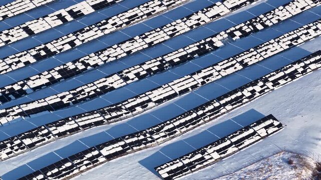 Aerial rise over a large solar panel farm in winter Latvia with rows of photovoltaic panels partially covered in snow, highlighting green energy generation challenges in cold climates