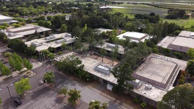 Aerial drone view slowly orbiting the modern architectural buildings and lush green trees of the Napa Valley College campus, located in the heart of Northern California's wine country