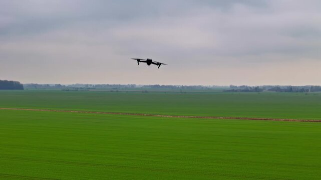 Quadcopter drone hovers and moves above vast green farmland rows under cloudy horizon in wide cinematic tracking shot across flat countryside