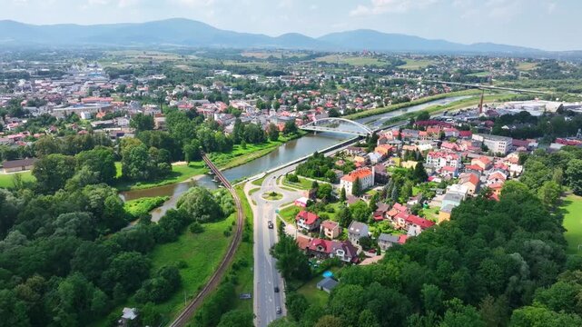 Cinematic aerial panorama of Zywiec, Poland, featuring the Sola river, modern bridge infrastructure, and the Beskid mountains. Captures urban development and natural beauty.
