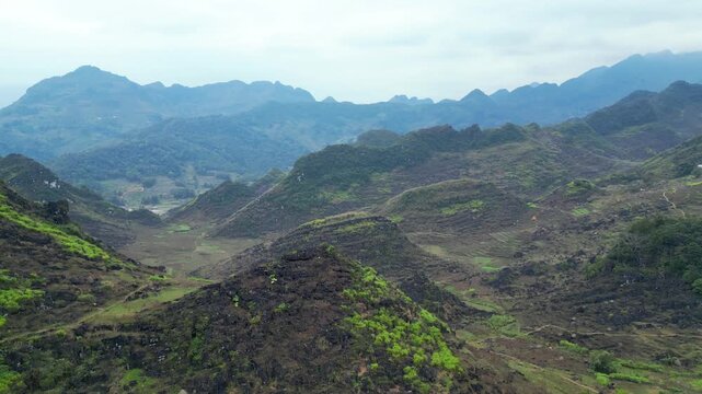 Panoramic drone view of rolling karst hills with terraced slopes and deep valleys under expansive hazy sky in Dong Van Karst Plateau Geopark Ha Giang Northern Vietnam