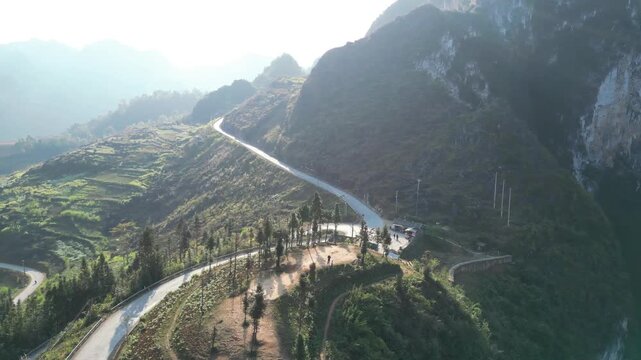 Aerial drone shot of winding cliffside road and scenic lookout above deep mountain valley in Ma Pi Leng Pass Ha Giang Loop Northern Vietnam with dramatic karst landscape