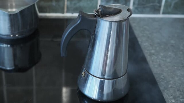 A moka pot brewing percolating fresh ground coffee with lots of steam on an induction hob with lots of steam leaking