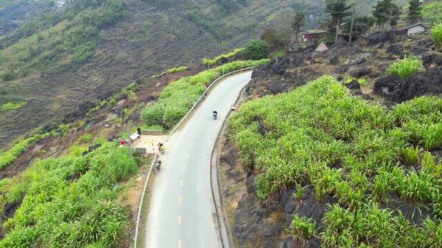 High angle aerial drone shot of lone motorcyclist riding along winding asphalt road through lush terraced hills in Dong Van Karst Plateau Geopark Ha Giang Northern Vietnam