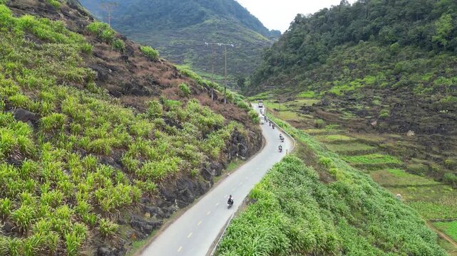 Aerial drone shot of motorcyclists riding along winding mountain road through rocky green terraces in Dong Van Karst Plateau Geopark Ha Giang Northern Vietnam