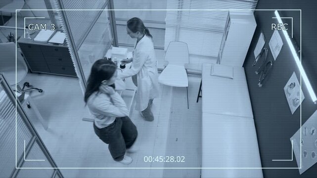 CCTV shot of young woman sitting down on couch after entering examination room with female physician who then putting on medical gloves and checking patients lungs with stethoscope