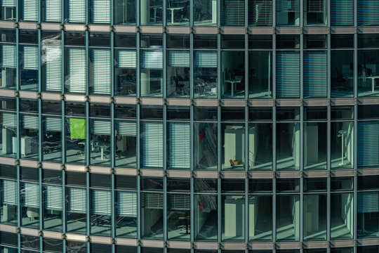 A modern glass facade of an office tower in Berlin - some of the windows have gray blinds pulled down, and one has a green roller shade