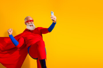 Naklejka premium Energetic senior superhero in bright red costume strikes a dynamic pose as he selfies against a yellow background