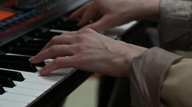 female pianist hands on black and white synthesizer keyboard, close-up view, young woman playing piano, professional musician