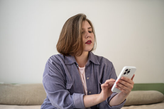 Plus size woman using smartphone on sofa at home, mobile lifestyle, messaging, online communication, social media, digital routine, modern living, body positivity.