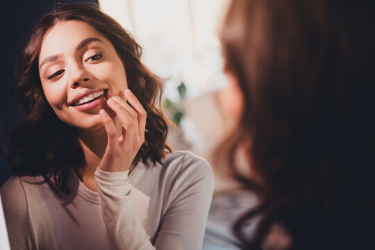 Young woman smiling at herself in a mirror, enjoying a quiet moment of beauty, self-care and confidence at home