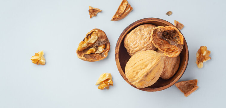 Roasted walnuts in wooden bowl with cracked walnuts on table, flat lay