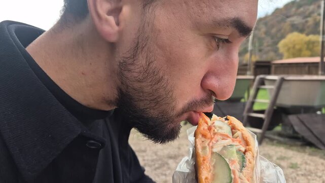 Man eating shawarma wrap outdoors enjoying street food lunch during autumn travel break