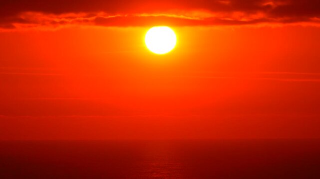 Sunset ocean sky time-lapse shows fiery red and orange sun setting over the vast sea horizon.
