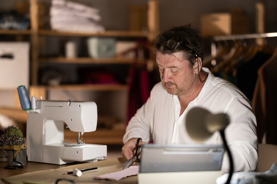 Middle-aged male dressmaker cutting cloth detail watching online lesson