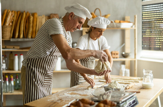 Elderly male chef and female skillfully kneads dough to bake delicious bread and croissants