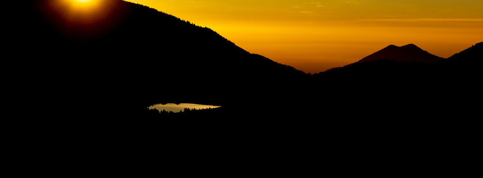 Landscape, tourism: Silhouette of mountains and a lake against a golden sunset sky, creating a sense of tranquility and destination. Luserna, Alpe Cimbra, Trentino, Italy.