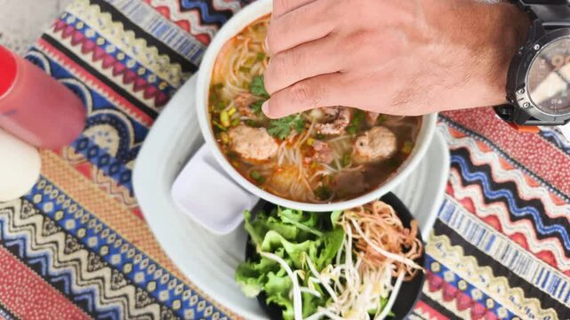 Authentic Bun Bo Hue captures hand squeezing fresh lime into spicy beef noodle soup. Vibrant greens and aromatic broth highlight traditional Vietnamese flavors. This authentic Bun Bo Hue meal.