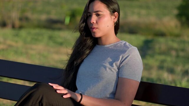 Young woman sitting on a park bench feeling unwell and holding her head