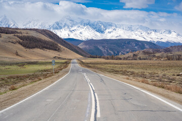 Fototapeta premium Asphalt road leading to snow-covered Akturu ridge in Kurai steppe valley Altai, Russia