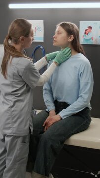 Vertical shot of female endocrinologist placing medical form on examination table and palpating girls neck during workday in reproductive center