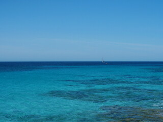 Obraz premium Vast sea with a small sailboat and rich blue tones. Minimalistic scene with large copy space.