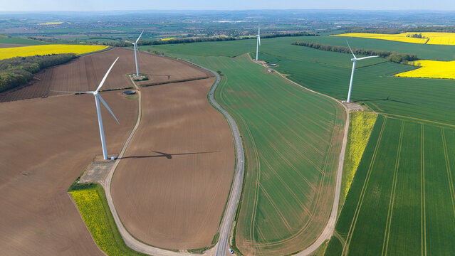 Onshore wind turbines generating clean energy over colourful agricultural fields, aerial view, United Kingdom.