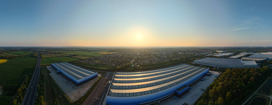 High angle aerial drone view of massive industrial warehouses and logistics distribution centers in warm golden sunlight UK