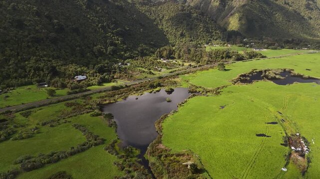 Lush green coastal plain with wetlands and farms near Barrytown on West Coast of New Zealand. Aerial backward