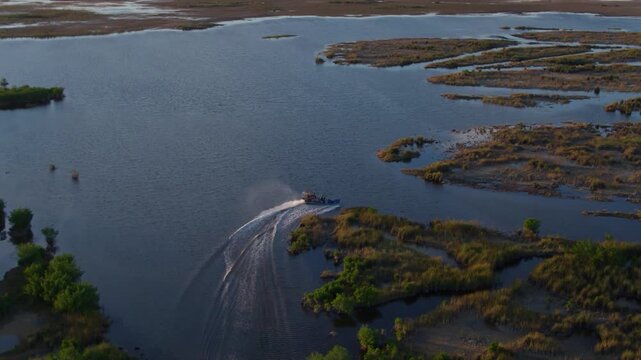 Cinematic drone shot of a fast-moving airboat navigating the lush sawgrass marshes and winding channels of the Florida Everglades.