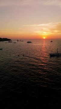 Vertical drone flyover at sunset over calm sea and anchored boats in Panglao, Bohol