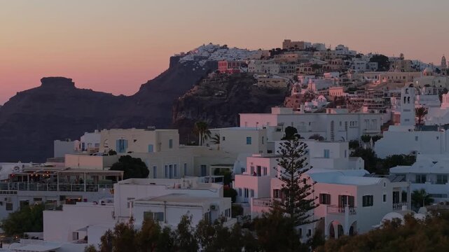 A lateral drone tracking shot of Fira, Santorini. Captured in warm summer afternoon light, the white houses gleam against the volcanic cliffs with the distant horizon in view.