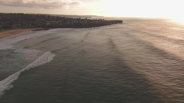 Beautiful 59 second drone footage flies forward over Maroubra Beach at sunrise as surfers wait for waves in the golden morning light while the sun reflects off the Pacific Ocean in Sydney
