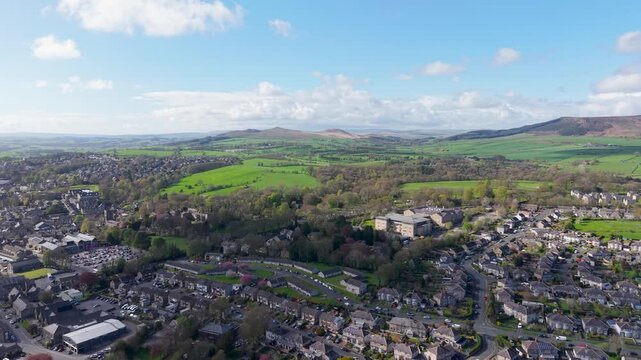 A forward drone flight over northern Skipton reveals the Skipton Building Society headquarters, residential streets and Aireville Park, with rolling moorland and blue skies stretching beyond.