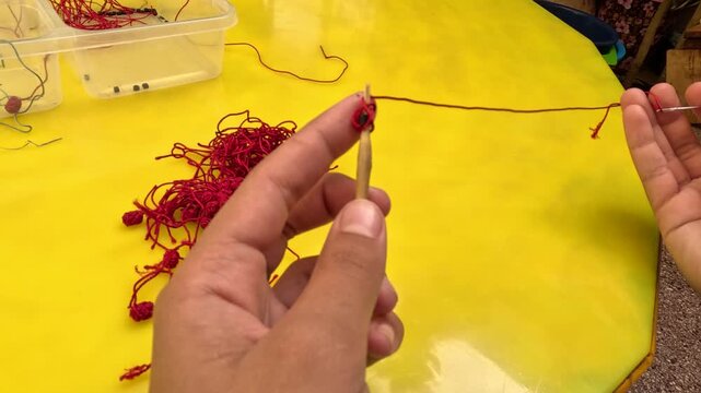 Close-up of Moroccan artisan making Aqad knots by hand using a hook tool. Traditional textile technique creating decorative buttons for caftans and djellabas, showcasing craftsmanship.