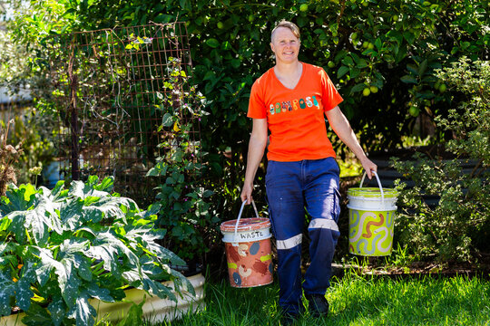 Australian woman in backyard garden carrying buckets for food scraps to compost