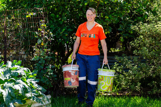 Australian woman in backyard garden carrying buckets for food scraps to compost