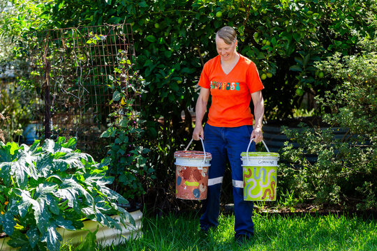 Australian woman in backyard garden carrying buckets for food scraps to compost