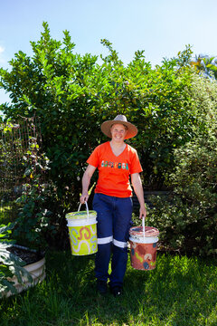 Australian woman in backyard garden carrying buckets for food scraps to compost