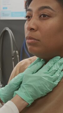 Vertical shot of gloved hands of anonymous endocrinologist palpating lymph nodes of Black woman