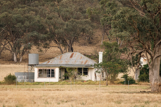 Dilapidated rural homestead with corrugated iron roof and water tanks in dry landscape