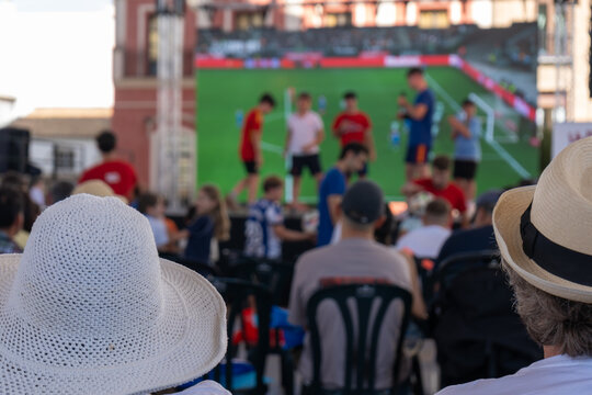 Audience watching football presentation on big screen at outdoor fan gathering in city square