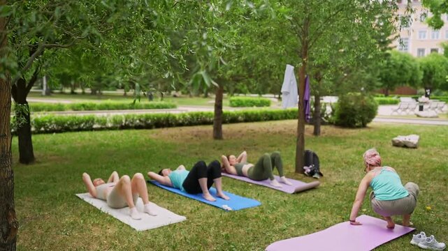 Group of women doing abdominal and core exercises on grass mats outdoors together during summer fitness class. Abs exercises, mats, group, fitness, outdoors, women.
