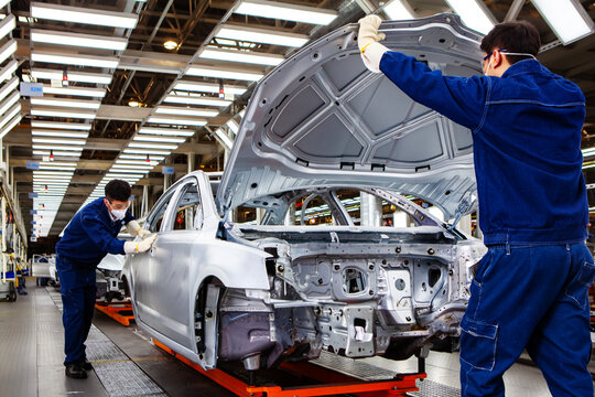 Two Asian workers are working on a car production line.