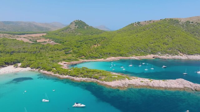 Aerial view of scenic Mallorca beach and turquoise bay with boats in Spain. Balearic Islands rocky coastline landscape in summer. Mediterranean nature and vacation destination. View from a drone.