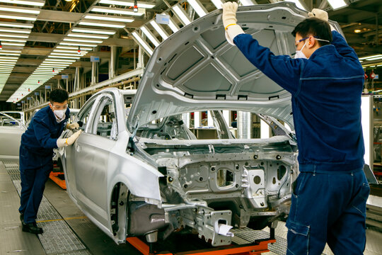 Two Asian workers are working on a car production line.