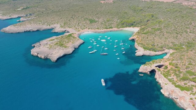 Aerial view of scenic Mallorca beach and turquoise bay with boats in Spain. Balearic Islands rocky coastline landscape in summer. Mediterranean nature and vacation destination. View from a drone.